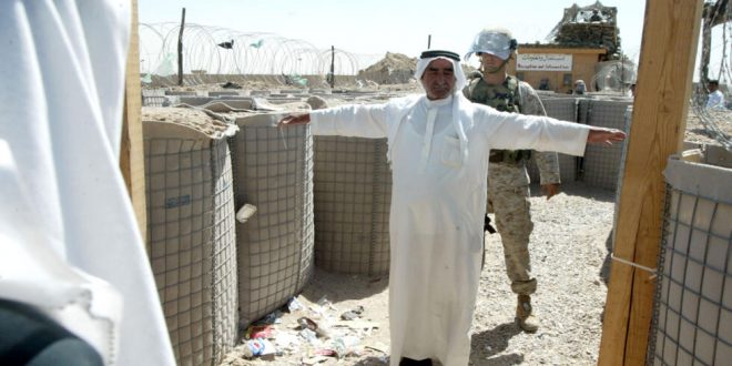 عنصر في مشاة البحرية الأمريكية يفتّش عراقيا لدى دخوله سجن أبو غريب لزيارة أحد أقربائه في مايو 2004. (أ ف ب)